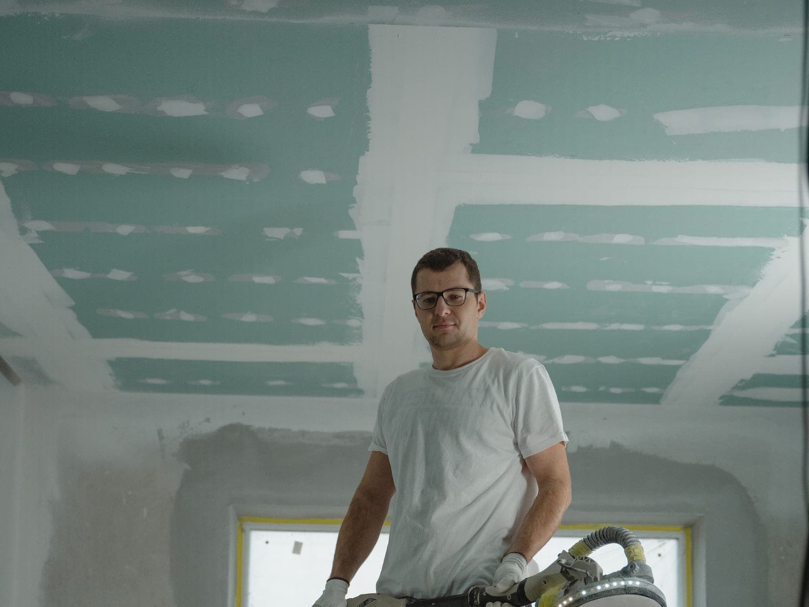 Plaquiste sur échasses ponçant les joints d'un faux plafond en plaques de plâtre